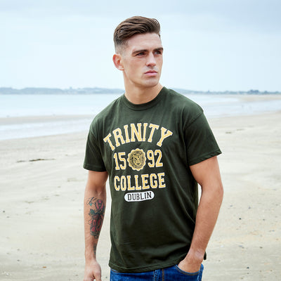 Man wearing a green 'Trinity College Dublin' t-shirt on a beach