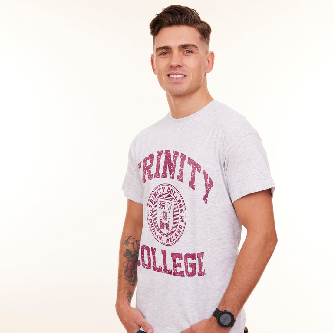 Man wearing a light grey t-shirt with 'Trinity College' printed on it against a white background